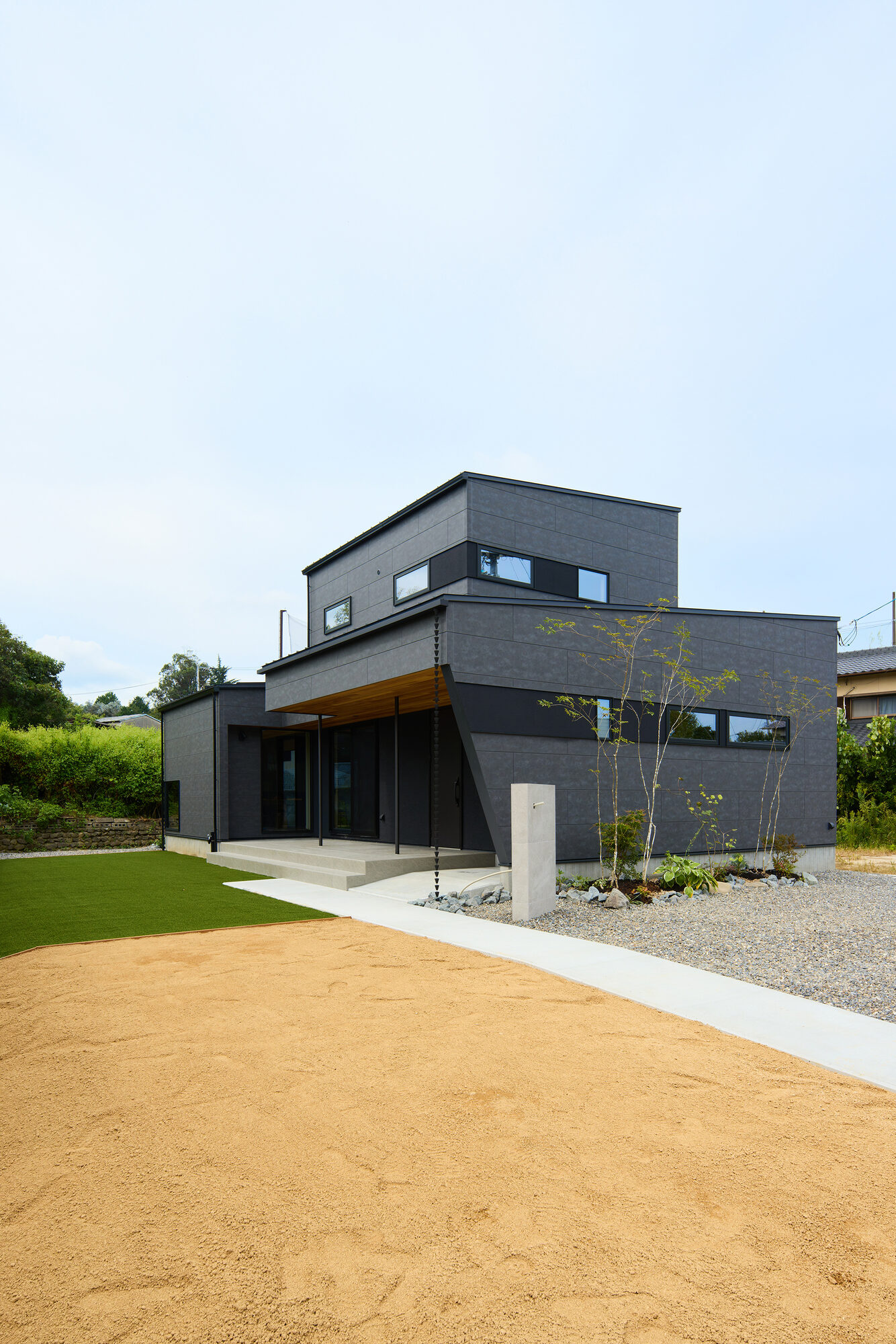 芝生と土の広い庭に面して建つ、黒い外観の家