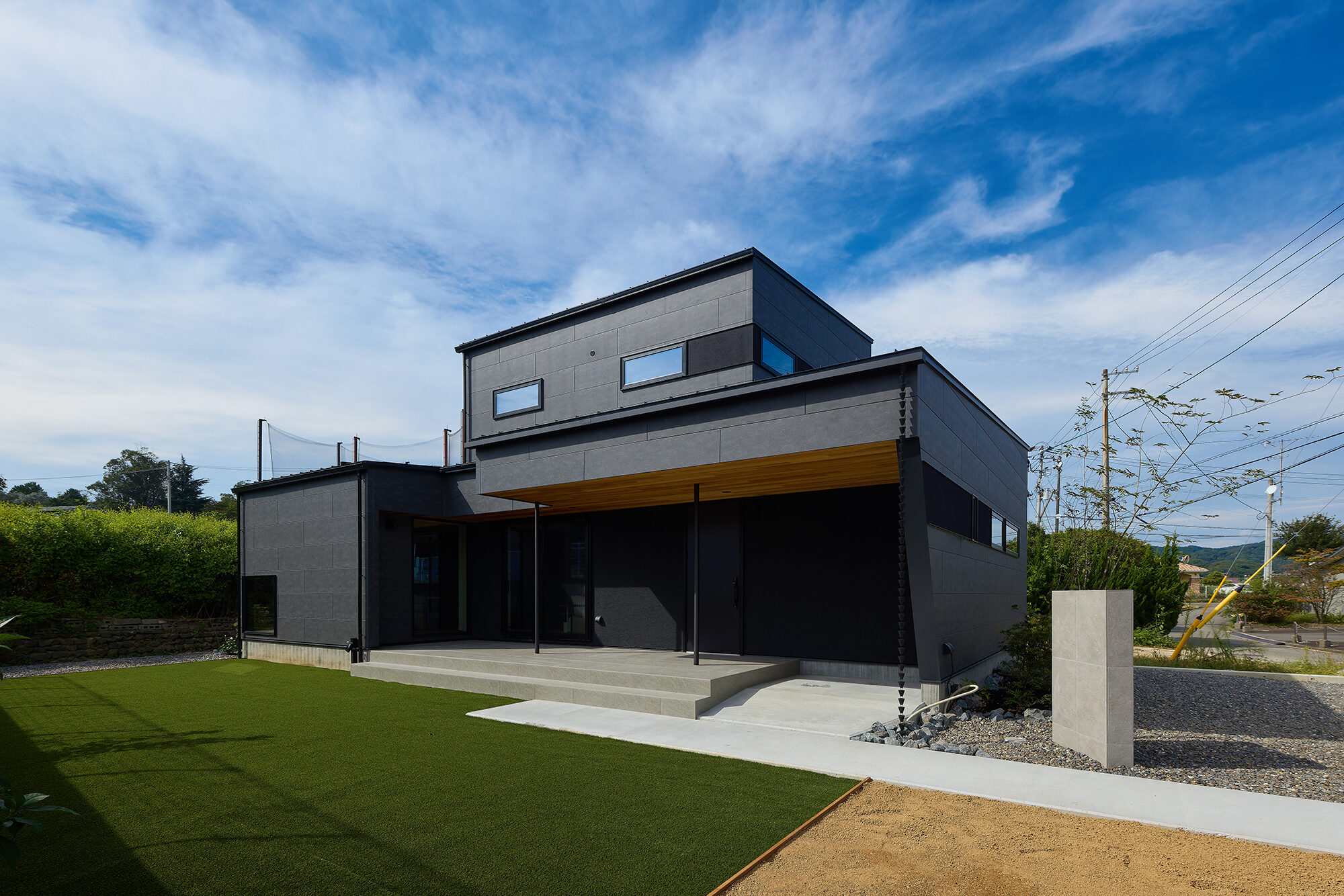 青空の下、黒い外壁と木の軒天をもつ住宅の外観