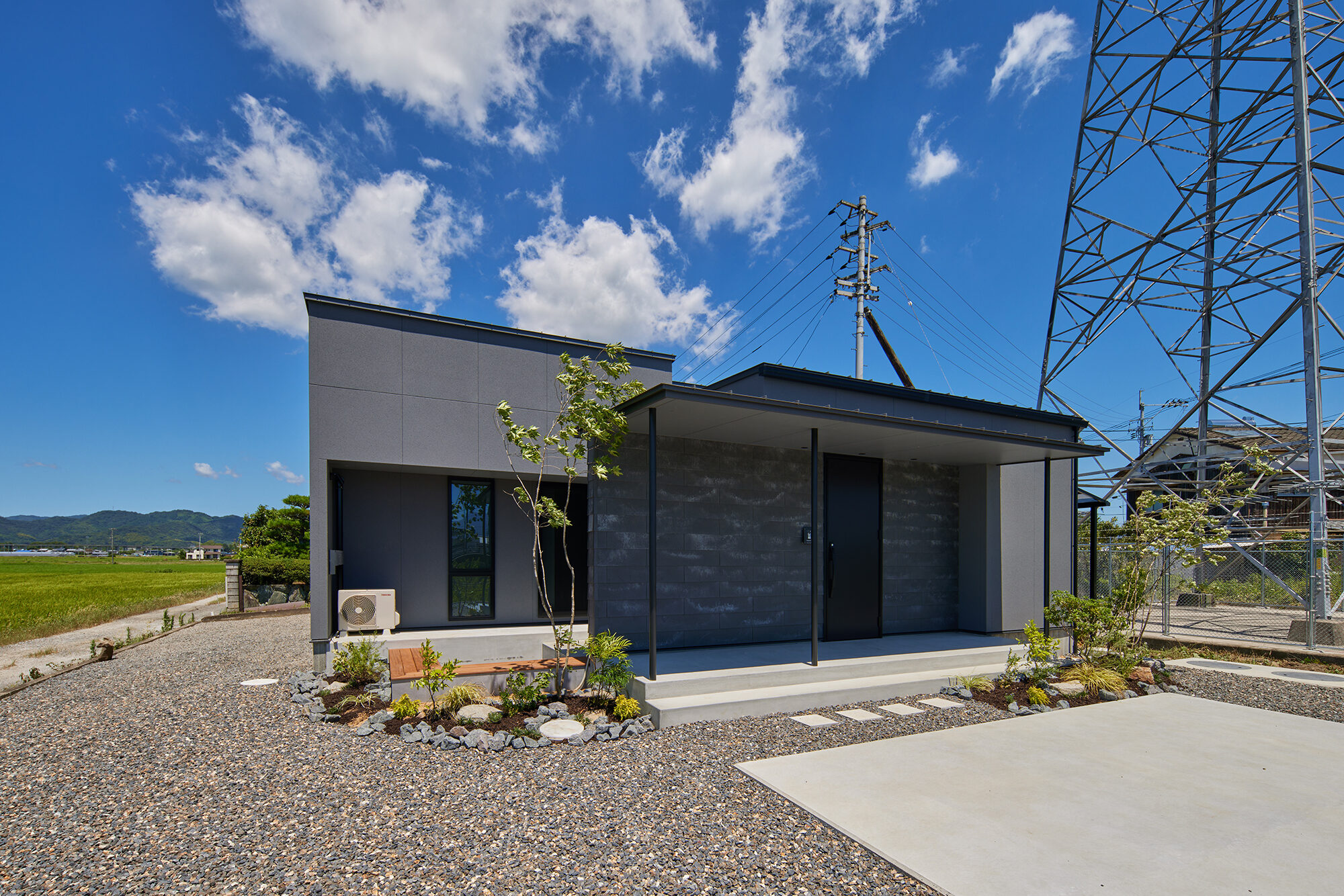 田畑の広がる敷地に建つ、石張りと黒い外壁の平屋