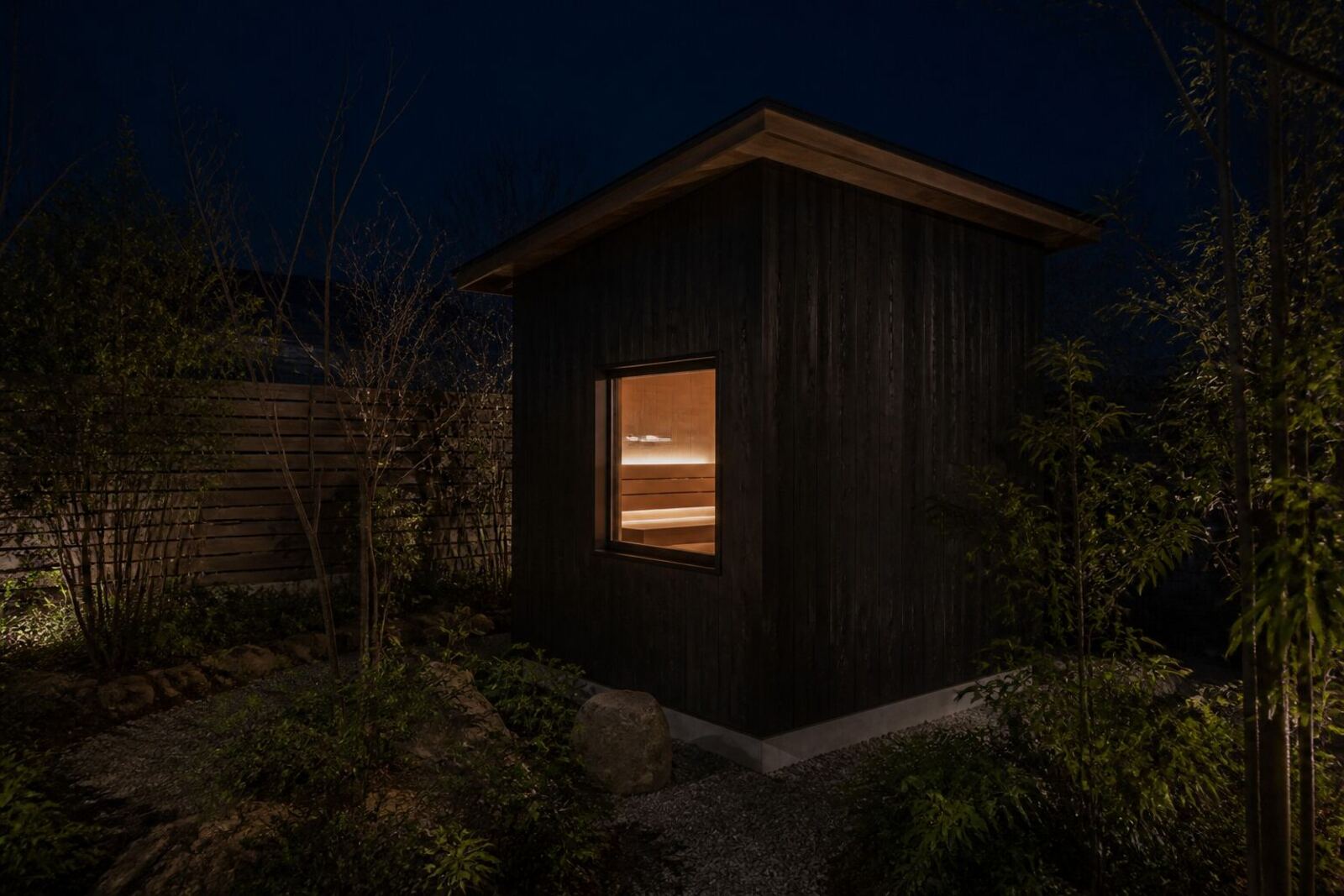 夜、庭に置かれた小屋型の屋外サウナから灯りが漏れている