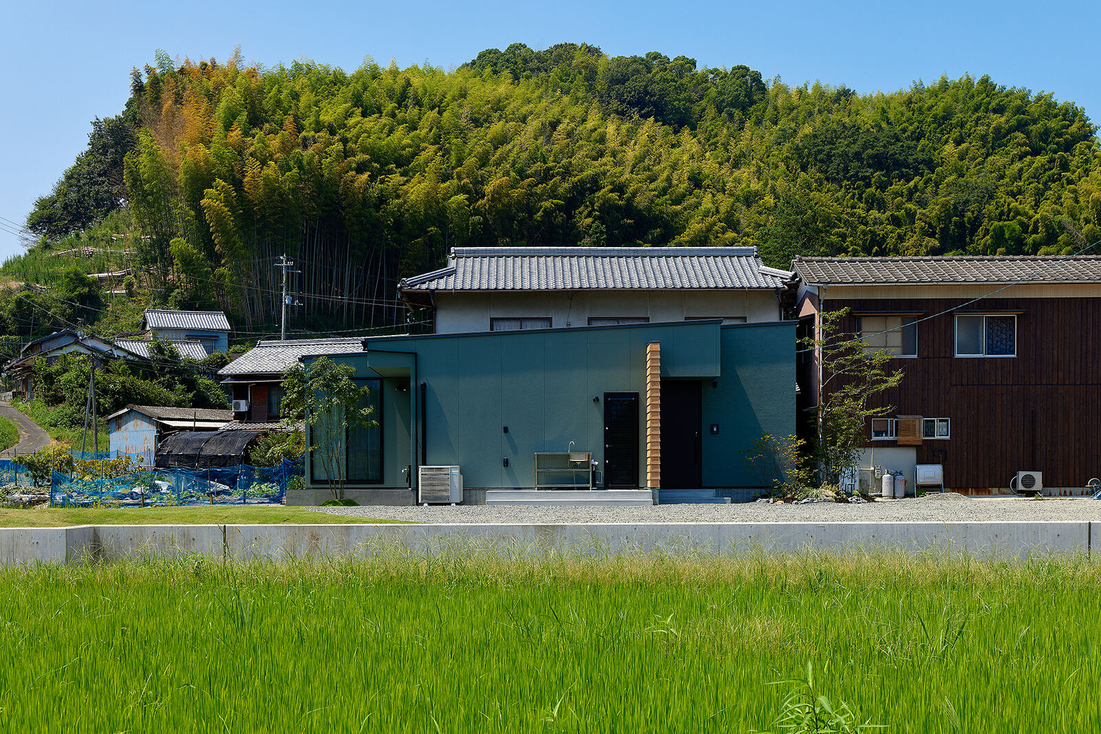 田んぼの向こうに横たわる、黒い平屋の外観